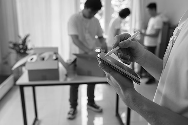 A manager of charity organisation taking notes on tablet computer while other volunteers packing boxes in the background