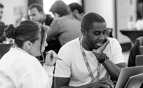 Two people wearing Equal Experts lanyards working together at a laptop in an open office.